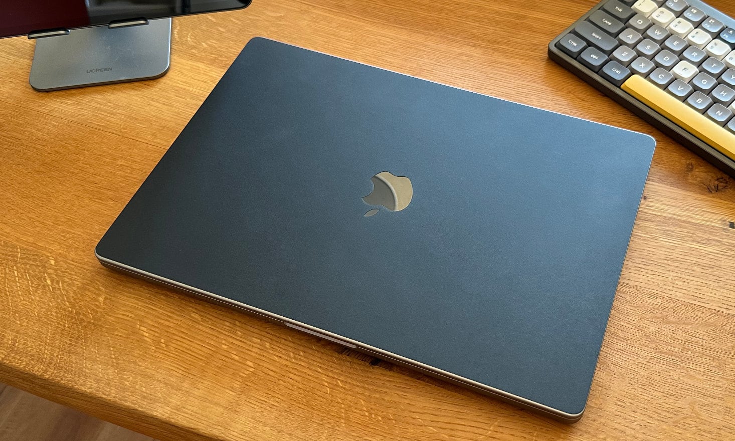閉じた状態のMacBook Pro 16インチがdbrandのマットブラックのスキンが貼られた状態で木目の見えるテーブルに置いてある。右上にはNuPhy Air75のカラフルなキーボードが見切れている